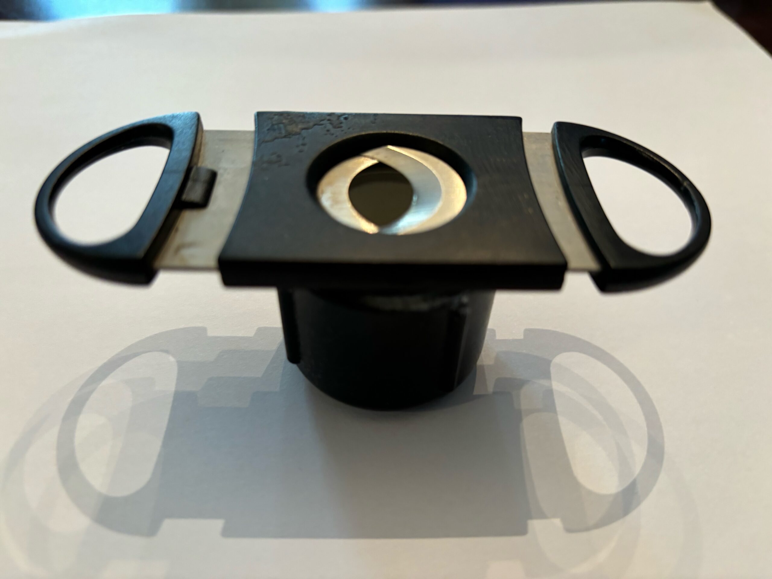 A black and silver cigar cutter rests on a white surface, showcasing its blades and circular opening for cutting cigars cleanly.